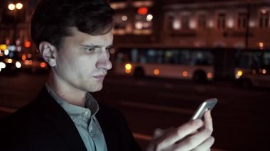 Genç casual giyimli adam gece cep telefonunu meşgul bir kentsel sokakta tarama