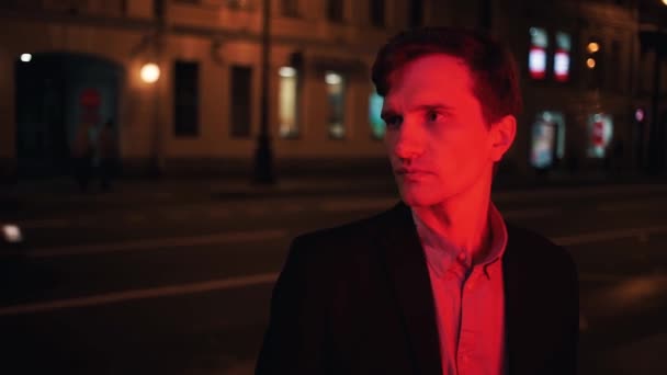 Портрет молодого чоловіка, освітлений червоним світлом, що стоїть на самоті вночі в місті — стокове відео