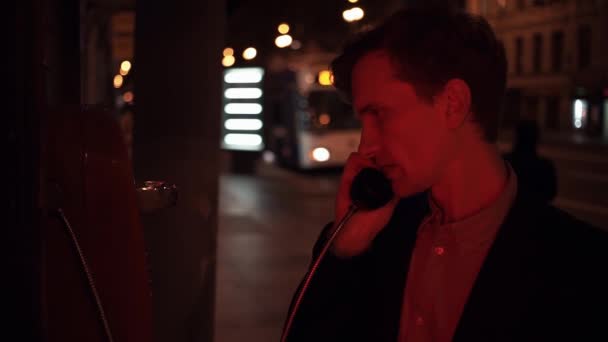 Young man using payphone at night in city srteet. Car city traffic at background — Stock Video