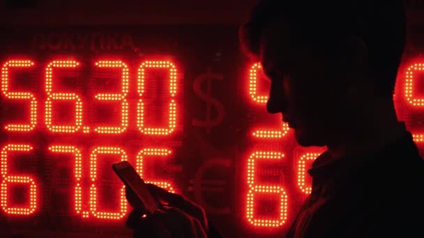 Homme utilisant un téléphone intelligent la nuit dans la ville debout près de l'affichage avec le taux de change . — Video