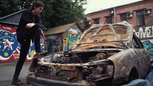 Jovem vestido de desgaste casual em pé no pára-lamas do carro queimado caiu — Vídeo de Stock