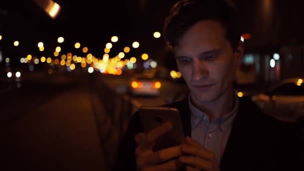 Junge, lässig gekleidete Geschäftsleute nutzen nachts Smartphone auf belebter Stadtstraße — Stockvideo