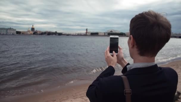 Příležitostné oblečený mladík pomocí přenosného počítače sedí na nábřeží. Práce venku — Stock video