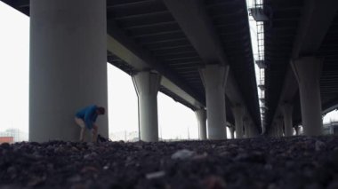 Genç adam yerdeki yolu köprüsü altında oturan smartphone kullanarak.