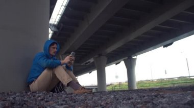 Toprak yolu köprüsü altında oturan smartphone kullanarak genç uzun yürüyüşe çıkan kimse