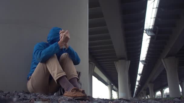 Un joven sin techo en el suelo bajo el puente de la carretera. Libertad viaje aventura tema — Vídeo de stock