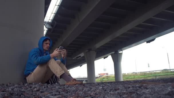 Hiker smartphone compras en línea con tarjeta de crédito sentado debajo del puente de carretera — Vídeos de Stock