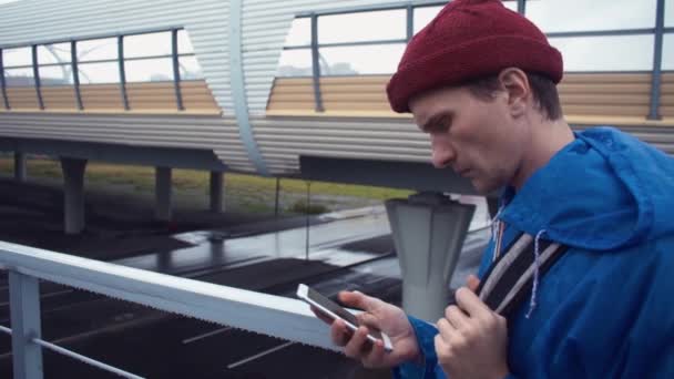 Jonge wandelaar gebruik van smartphone staande op de verkeersbrug. Weg snelweg op achtergrond — Stockvideo