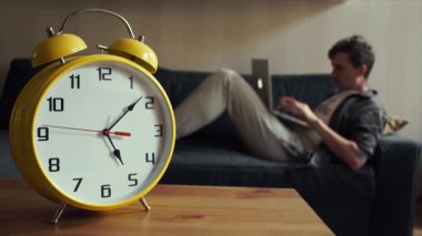 Genç öğrenci evde kanepede otururken dizüstü bilgisayar kullanarak. Büyük sarı Saat işliyor