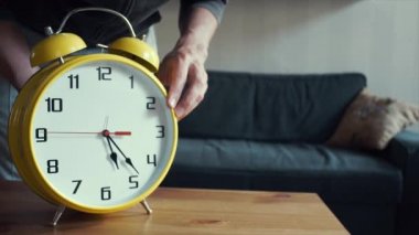 Genç adam doğru zaman üzerinde büyük sarı saatini ayarlar. Oturma odası iç