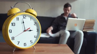 Genç öğrenci evde kanepede otururken dizüstü bilgisayar kullanarak. Büyük sarı Saat işliyor