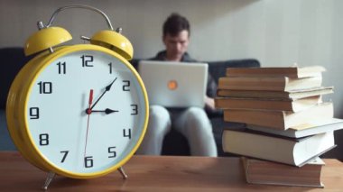 Evde kanepede otururken dizüstü kullanan genç adam. Büyük sarı Saat işliyor