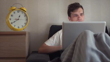 Genç öğrenci evde kanepede otururken dizüstü bilgisayar kullanarak. Büyük sarı Saat işliyor