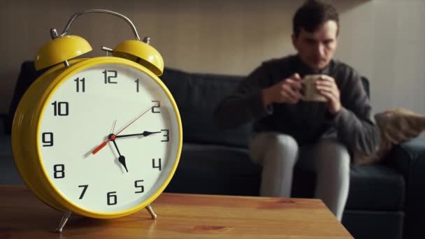 Il giovane mette la tazza di tè sullo scaffale. Grande orologio giallo sta ticchettando — Video Stock