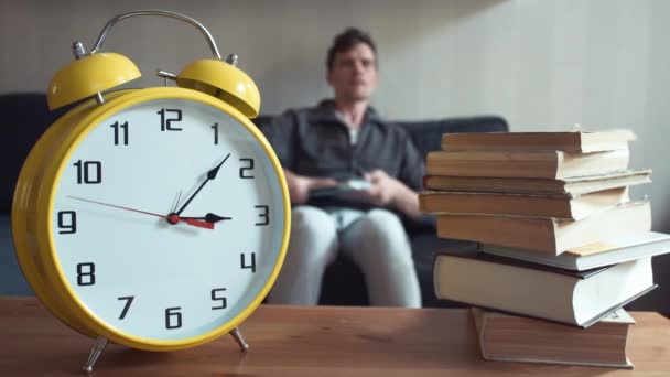 남자 집에서 책을 읽고 하는 소파에 앉아 노트북을 사용 하 여. 노란색 시계가 똑 딱이다 — 비디오