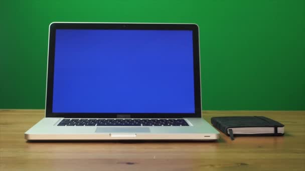 Laptop with a green screen and black notepad on table. Green screen background — Stock Video