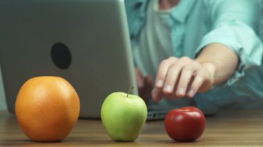 Portakal, elma ve domates önünde masada dizüstü bilgisayar kullanan adam