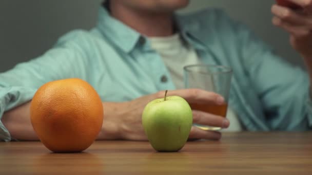 Naranja, manzana y tomate en la mesa frente al hombre que bebe jugo — Vídeos de Stock