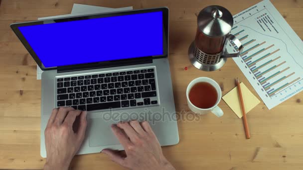 Vista superior da mesa com material de escritório. Mãos masculinas usando laptop com tela verde — Vídeo de Stock