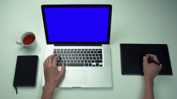 Vista superior de las manos masculinas utilizando la ficha gráfica y el ordenador portátil con pantalla verde en el escritorio blanco — Vídeo de stock