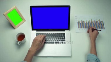 Üstten Görünüm erkek el ile yeşil ekran dizüstü kullanarak basılı grafikler ile çalışma