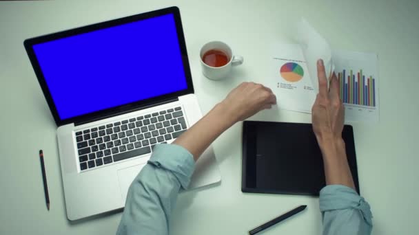 Bovenaanzicht mannelijke handen werken met gedrukte grafieken laptop met groen scherm — Stockvideo