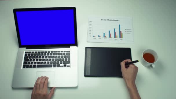 Männliche Hände mit Grafiktab und Laptop mit grünem Bildschirm am weißen Schreibtisch — Stockvideo