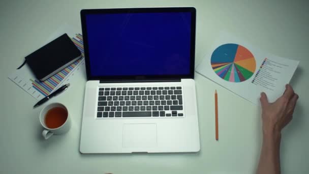 Top vista mãos masculinas trabalhando com gráficos impressos usando laptop com tela verde — Vídeo de Stock