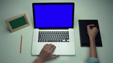 Üstten Görünüm erkek ellerini beyaz masada yeşil ekranlı grafik sekmesini ve dizüstü bilgisayar kullanarak