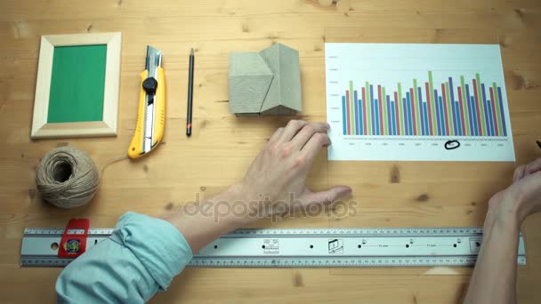 Männliche Hände arbeiten mit gedruckten Diagrammen und machen sich Notizen mit Filzstift am Holztisch. — Stockvideo