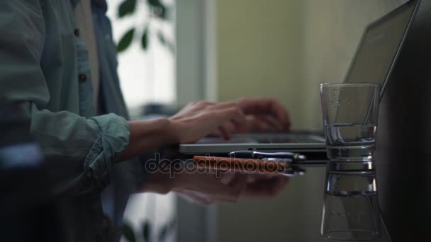 Un vaso de agua, lápiz, bloc de notas y pegajoso en el escritorio. Hombre de negocios usando portátil — Vídeos de Stock