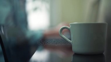Erkek el beyaz Kupası masadan alarak kapatın. Dizüstü bilgisayarda yazarak adam