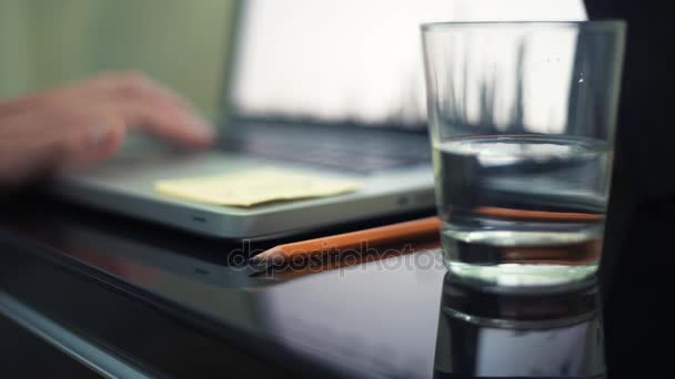 水とテーブルの上の鉛筆のガラスのクローズ アップ。カフェでノート パソコンを使って若い男. — ストック動画