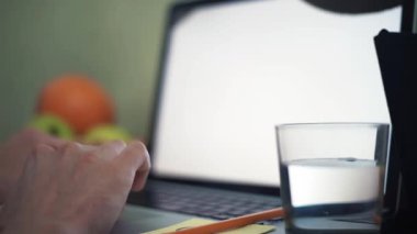 Laptop klavye üzerinde genç adam elinde. Su ve kalem masada