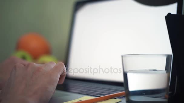 Руки молодого чоловіка на клавіатурі ноутбука. Склянка води та олівця на столі — стокове відео