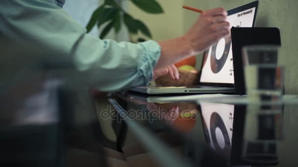 Jeune homme utilisant un ordinateur portable dans un café. Verre d'eau, bloc-notes et crayon sur la table — Video