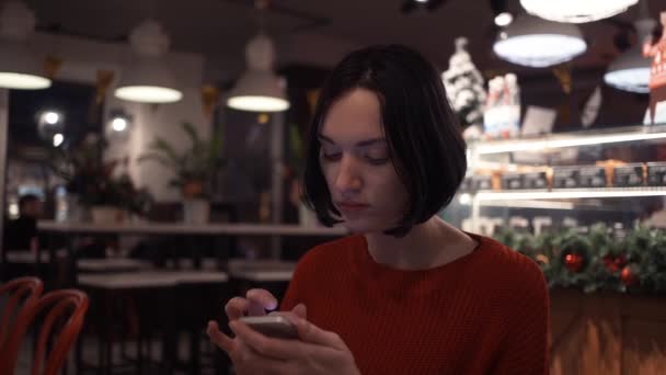 Mulher jovem bonito mensagem de texto usando smartphone sentado no café . — Vídeo de Stock