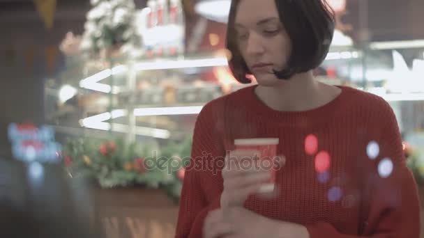 Retrato de una joven atractiva mujer usando un teléfono inteligente sentado en la cafetería. Tiempo de Navidad — Vídeo de stock