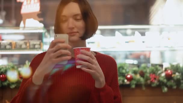Милая молодая женщина улыбается, используя смартфон, делая селфи, сидя в кафе — стоковое видео