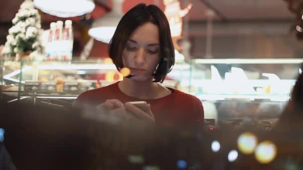 Mujer joven riendo usando teléfono inteligente chat en línea sentado en la cafetería . — Vídeos de Stock