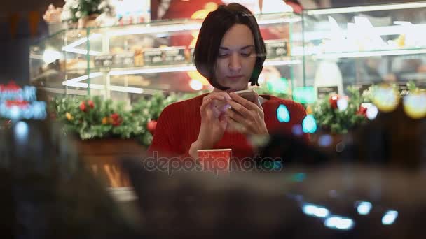 Hermosa joven sonriendo usando teléfono inteligente chat en línea sentado en la cafetería — Vídeos de Stock