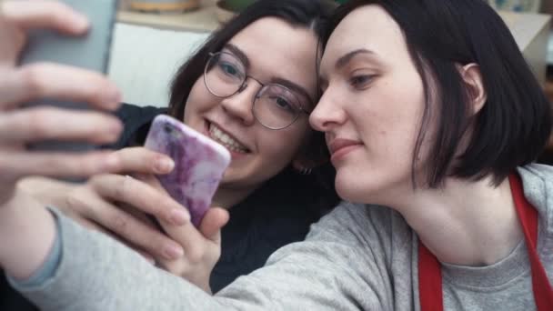 两个滑稽的女孩拿自拍在手机上躺在家里的沙发上 — 图库视频影像