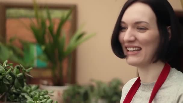 Junge Gärtnerin in roter Schürze im Gespräch mit jemandem im Gewächshaus. — Stockvideo