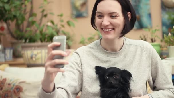 Jong meisje selfie met schattig zwarte huisdier chihuahua schoothondje nemen in woonkamer — Stockvideo