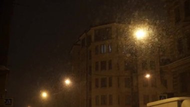 Kentin güçlü kar yağışı gece. Büyük kar taneleri ışıklı lamba düşüyor.