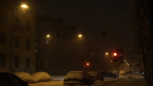 Salju lebat turun di kota pada malam hari. Snowflakes menerangi lampu jatuh di jalan — Stok Video