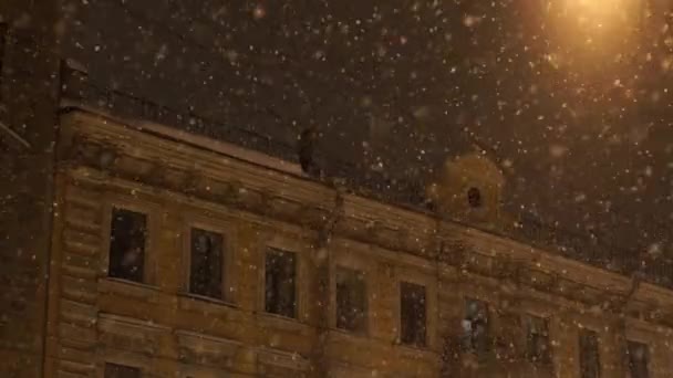 Чоловік проливає сніг з даху будинку. Сильні снігопади вночі в місті — стокове відео