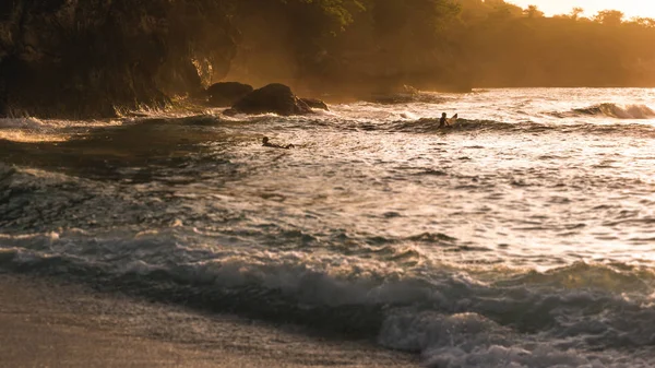 As crianças locais de surf nas ondas na luz do pôr do sol, bela Baía de cristal, Nusa Penida Bali — Fotografia de Stock