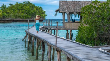 Sarışın kız kalmayı bir aile yanı mavi okyanus içine bakarak Gam Adası, Batı Papua, Raja Ampat, Endonezya ahşap iskele