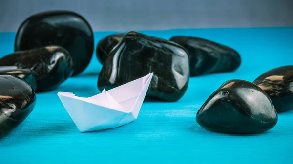 Ensam vitboken fartyg mellan abstrakt svart Rock stenar på blå bakgrund — Stockfoto